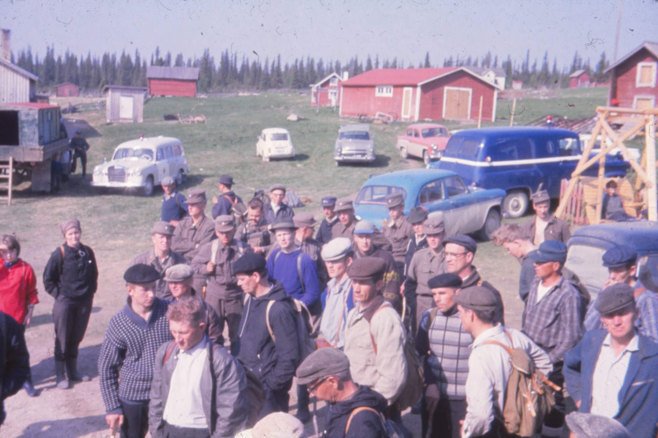 Valokuva 60-luvulta. Joukko vapaaehtoisia etsijöitä kokoontuneina maalaistalon pihaan.